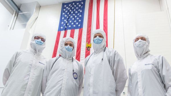Engineers in cleanroom suits posing with the American flag.