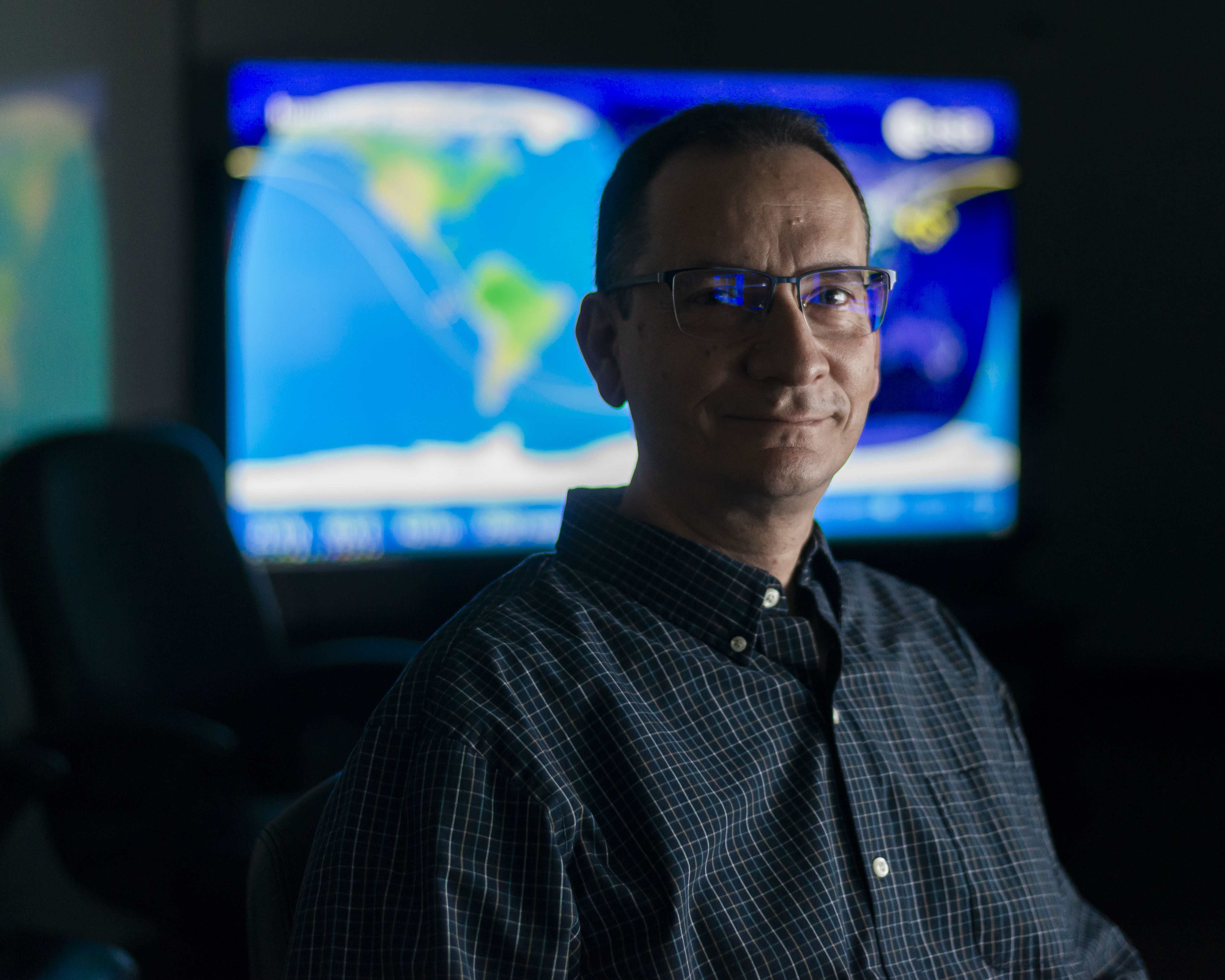 An Engineer sits in the AWE mission operations center with data streaming behind him.