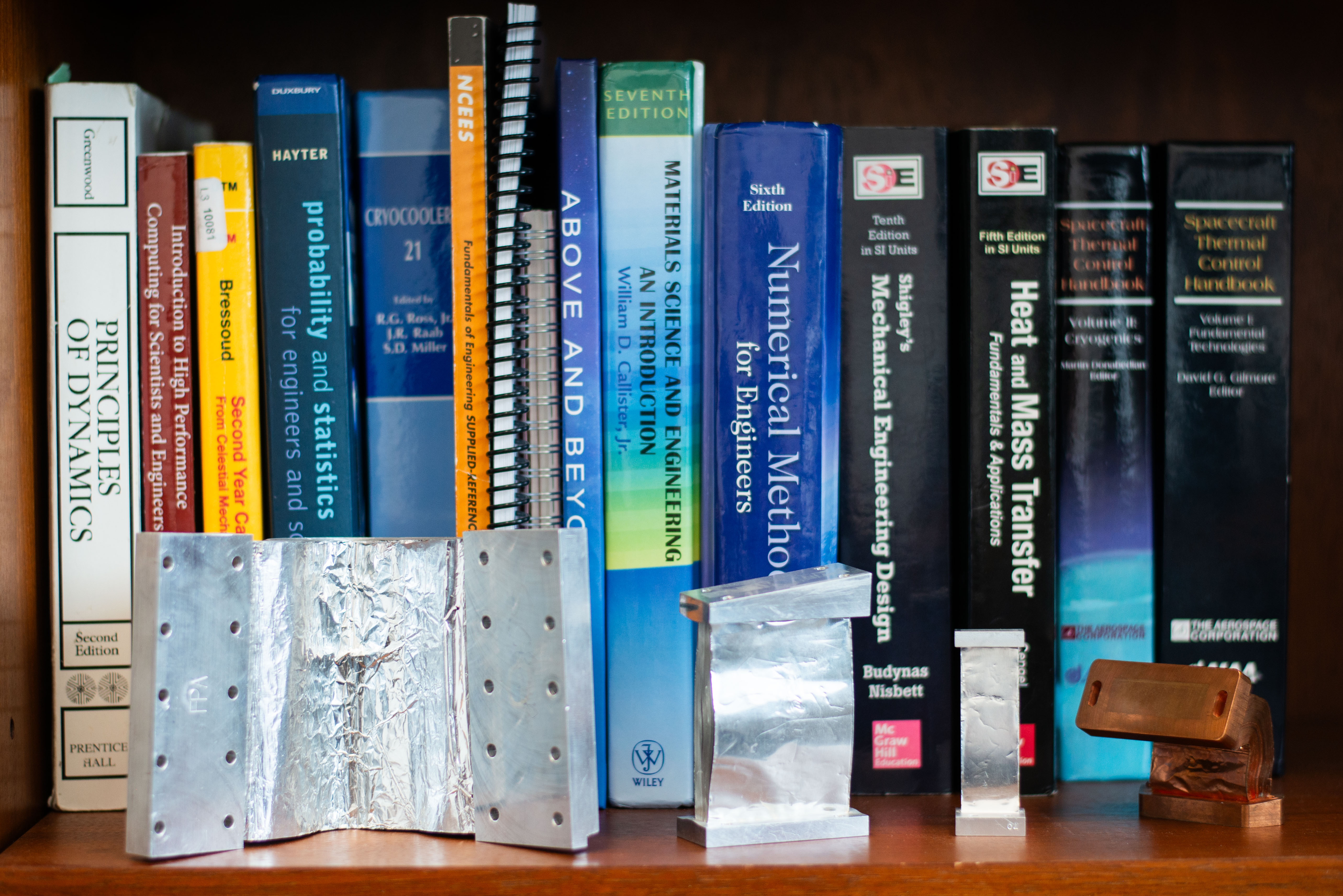 A collection of Matt's thermal strap designs and technical books on display on an office shelf.